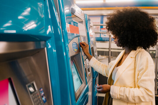 Woman with Afro hairstyle using ticket vending machine at subway station
