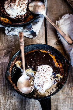 Frying pans with chocolate chip cookies covered with ganache topping and whipped cream