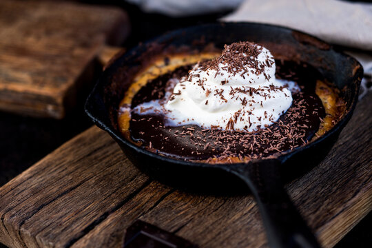 Frying pan with chocolate chip cookies covered with ganache topping and whipped cream