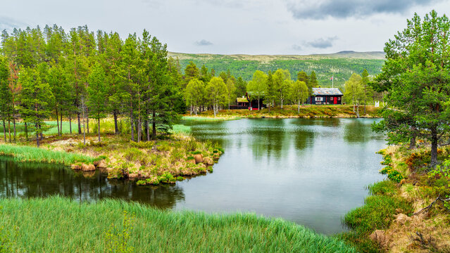 Norway, Innlandet, Lake in Rondane National Park with secluded hut in background