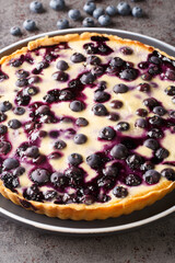 Traditional Finnish blueberry pie has a layer of blueberries are buried in a creamy custard topping on a crust close-up in a plate on a table. Vertical