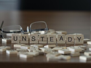 Unsteady word or concept represented by wooden letter tiles on a wooden table with glasses and a book - obrazy, fototapety, plakaty