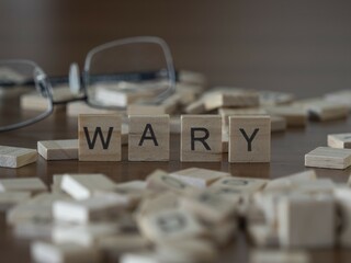 Wary word or concept represented by wooden letter tiles on a wooden table with glasses and a book