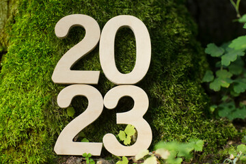 wooden numbers 2023 against a on a green background of moss. happy new year 2023 background banner...