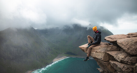Solo hiker admiring the view on top of a mountain with his feet in the void. Panorama of Ryten in Lofoten in Norway. Success symbol