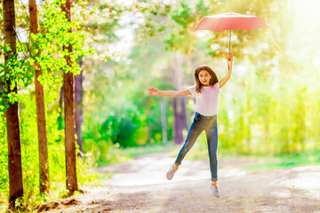 Girl teenager with a red umbrella jumps in the summer forest. Bright sunny day