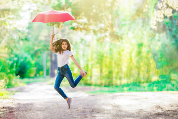 Girl with a red umbrella jumps in the summer forest. Bright sunny day