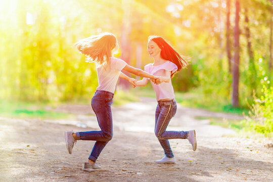 Two cheerful girlfriends are spinning holding hands, on a walk in the summer forest