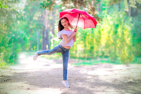 Teen girl flying with a red umbrella in the summer forest. Bright sunny day