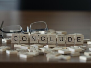 Conclude word or concept represented by wooden letter tiles on a wooden table with glasses and a book