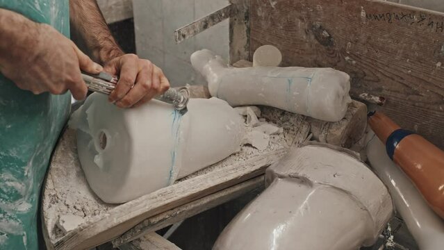 High angle of unrecognizable craftsman carefully cutting extra plastic after demolding prosthetic leg socket