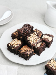 Homemade chocolate fudge brownie with mix topping, close up, served on plate, isolated on white background. Selective focus image.
