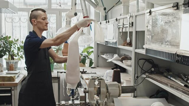 Young adult professional craftsman putting stocking on human hip plaster cast in prosthetic production workshop