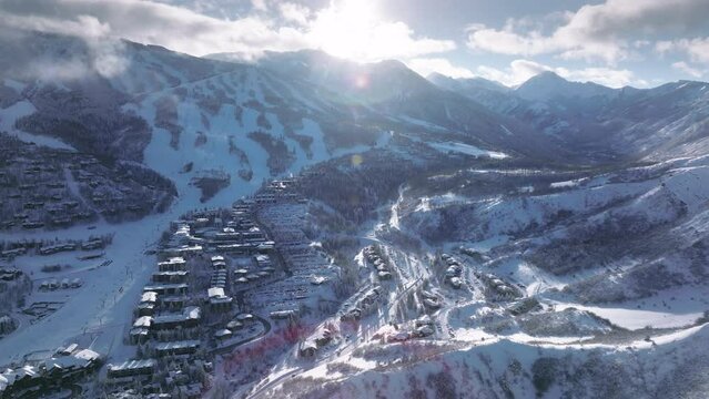Aerial view Aspen Snowmass on cold sunny winter day. Drone flying above world famous winter ski resort with expensive property houses and resort hotels with ski slopes and lifts, sun through clouds 4K