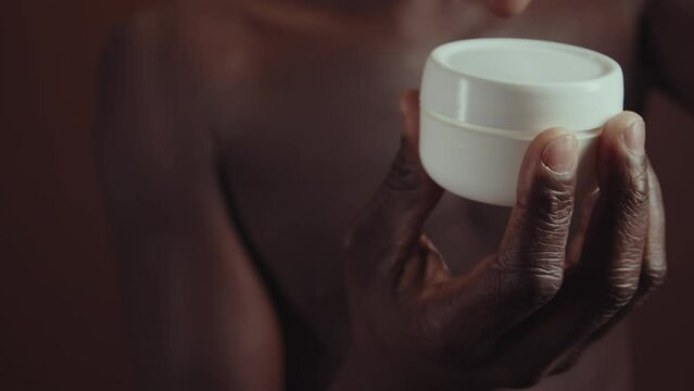 Selective focus close-up slowmo of unrecognizable African American man opening moisturizing cream jar