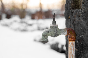 Old rusty retro outdoor garden faucet without valve stands outside in snowy garden or park near forest at sunset on snowy winter day. Season weather specific, hobby