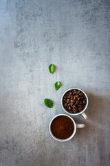 Zwei Tassen mit Kaffee Pulever und Bohnen auf einem grauen Tisch. Flat lay.