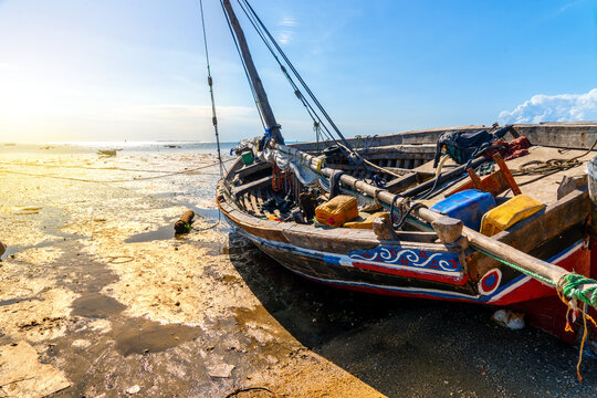 beached traditional wooden sailing dhow on the mud flats of the outgoing tide against a distant ocean horizon
