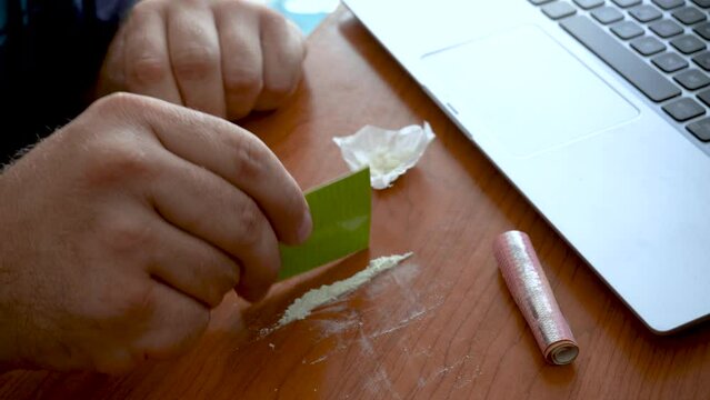 Man preparing a cocaine line in the office next to the computer.