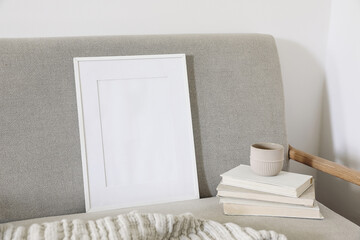 Empty wooden vertical picture frame mockup. Cup of coffee on pile of old books. Midcentury linen sofa. White wall background. Home office concept. Scandinavian interior design. Artistic display.