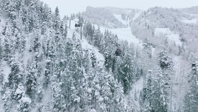 Aspen Mountain Ski and Snowboard Lift Gondola in Colorado Aerial USA. 4K aerial drone flying fast above ski cabins riding between scenic snow covered trees with mountain slopes view on cold winter day