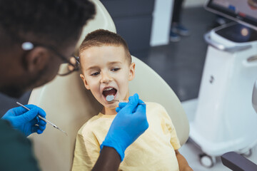 Shot of a young little boy lying down on a dentist chair while getting a checkup from the dentist. Dentist examining a patient's teeth in dentist office. People, stomatology and health care concept.