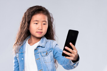 Fototapeta premium Cute girl child makes selfie. Device technology. On a light background in the studio