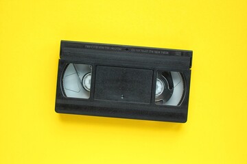 Obraz premium Black VHS videotape recorder cassette on yellow background. Old obsolete technology for tape recording and watching media movies. Retro, vintage, history, nostalgia concept. Top view, flat lay