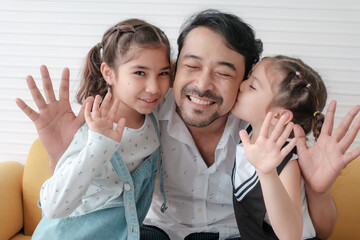Two daughters kiss their father's cheek and hug her father.
