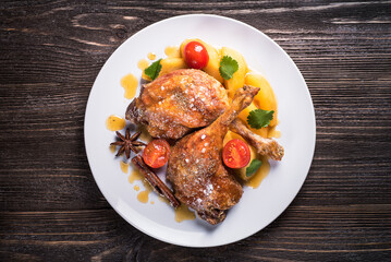 Duck legs with apples in orange sauce on a wooden background