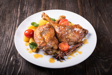 Duck legs with apples in orange sauce on a wooden background