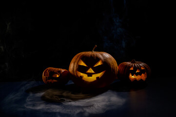 Pumpkins with carved grimaces and candles inside in the dark for halloween. Jack o latern in smoke.