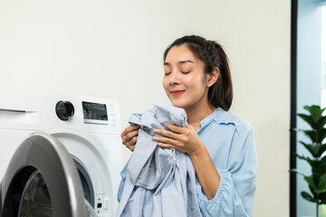 Happy housewife opens the front of the washing machine and smiles to receive the laundry that has...