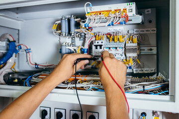 Adult electrician builder engineer testing and screwing equipment in fuse box and repairing of...