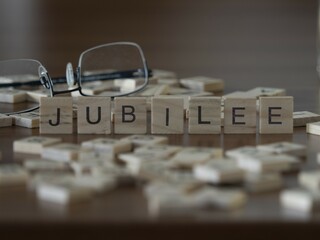 Jubilee word or concept represented by wooden letter tiles on a wooden table with glasses and a book
