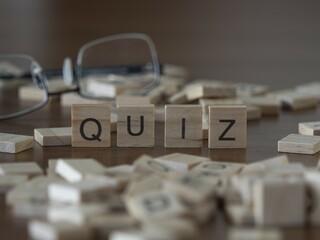 Quiz word or concept represented by wooden letter tiles on a wooden table with glasses and a book