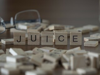 Juice word or concept represented by wooden letter tiles on a wooden table with glasses and a book