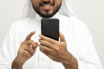 Portrait of arabic man with kandura dress using cellphone on isolated white background. Arab business people holding smartphone.