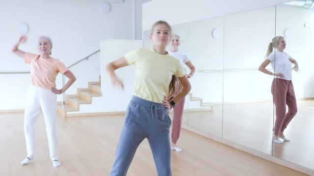 Positive teen girl with family doing aerobics exercises with group of people in dance center