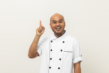 Smiling Young handsome asian man chef in uniform standing pointing finger on isolated blank space for text menu. Cooking indian man Occupation chef or baker People in kitchen restaurant and hotel.