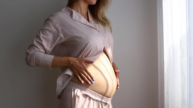 Happy pregnancy. Close up shot pregnant woman in pajamas stroking her big belly, caressing her unborn baby