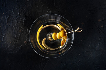 Martini, a glass with spicy olives on a toothpick, on a black background. Alcoholic cold drink, overhead shot