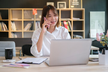 Young business woman talking on mobile phone, consulting client while working with laptop in the office.