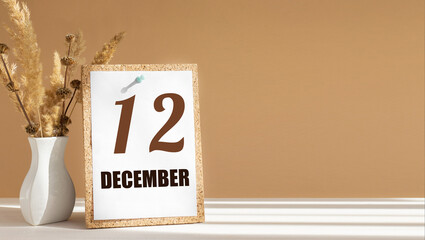 december 12. 12th day of month, calendar date.White vase with dead wood next to cork board with numbers. White-beige background with striped shadow. Concept of day of year, time planner, winter month