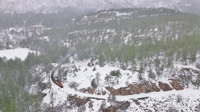 Train at winter day in Colorado mountain canyon with evergreen fir forest. Snowing in North America Aerial View. Drone flying above green forest. Popular tourist attraction on winter Christmas Durango