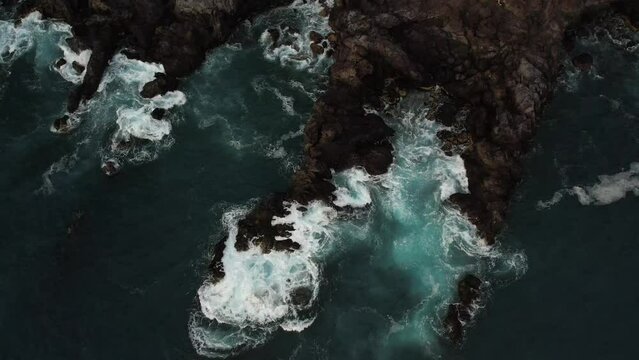 Top down view of rugged rocky shoreline in Tenerife. Atlantic Ocean crashing into dark volcanic rocks. Drone footage in 4K, 48fps (slow motion option). Turbulent water in Canary Islands.