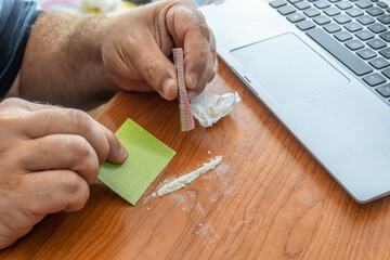 Man preparing a coacine line in the desk, next to the laptop. 