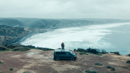 Two friends arrived with van to an epic camping location. Travelling with van in cold scandinavian country. Wanderlust millennial vanlife lifestyle. Aerial drone shot of camper van on edge of cliff