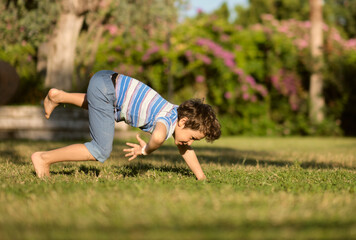 Fototapeta na wymiar Mischievous preschooler boy somersaults on sand grass in the park.