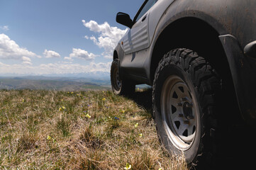 Fototapeta na wymiar SUV wheel on the off-road adventure trail against the backdrop of mountains in the clouds